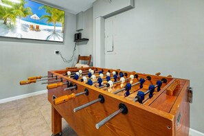 Ein Kicker-Tisch aus Holz in einem Raum mit einem Strand-Motiv an der Wand.