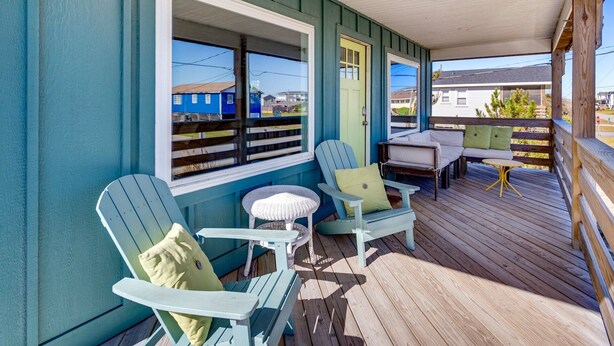 Un porche cubierto con sillas Adirondack y una pequeña mesa, con vistas a una zona residencial.