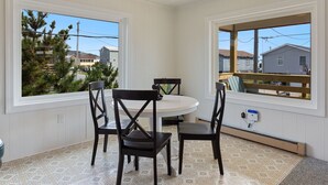 Un comedor con una mesa redonda y cuatro sillas, amplias ventanas con vistas a casas y árboles, y suelo de baldosas.