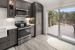 Enjoy cooking in this well-equipped kitchen with sleek cabinetry, stainless steel appliances, and a sliding glass door leading to a deck with a view.