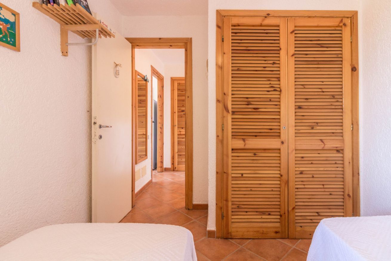 Un couloir avec des portes en bois, un lit et une étagère remplie d’objets.