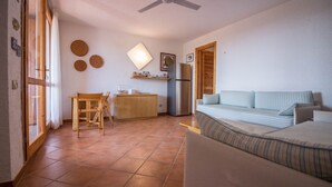 Una habitación pequeña con cama, escritorio, silla, refrigerador y ventilador de techo.