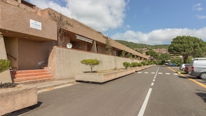 Un edificio con un cartel que dice 'LE PISCINE', un estacionamiento y una carretera que se dirige hacia un paisaje montañoso.