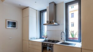 Una cuina moderna amb fogó a gas, forn, campana extractora d'acer inoxidable i una finestra amb vista a un edifici.