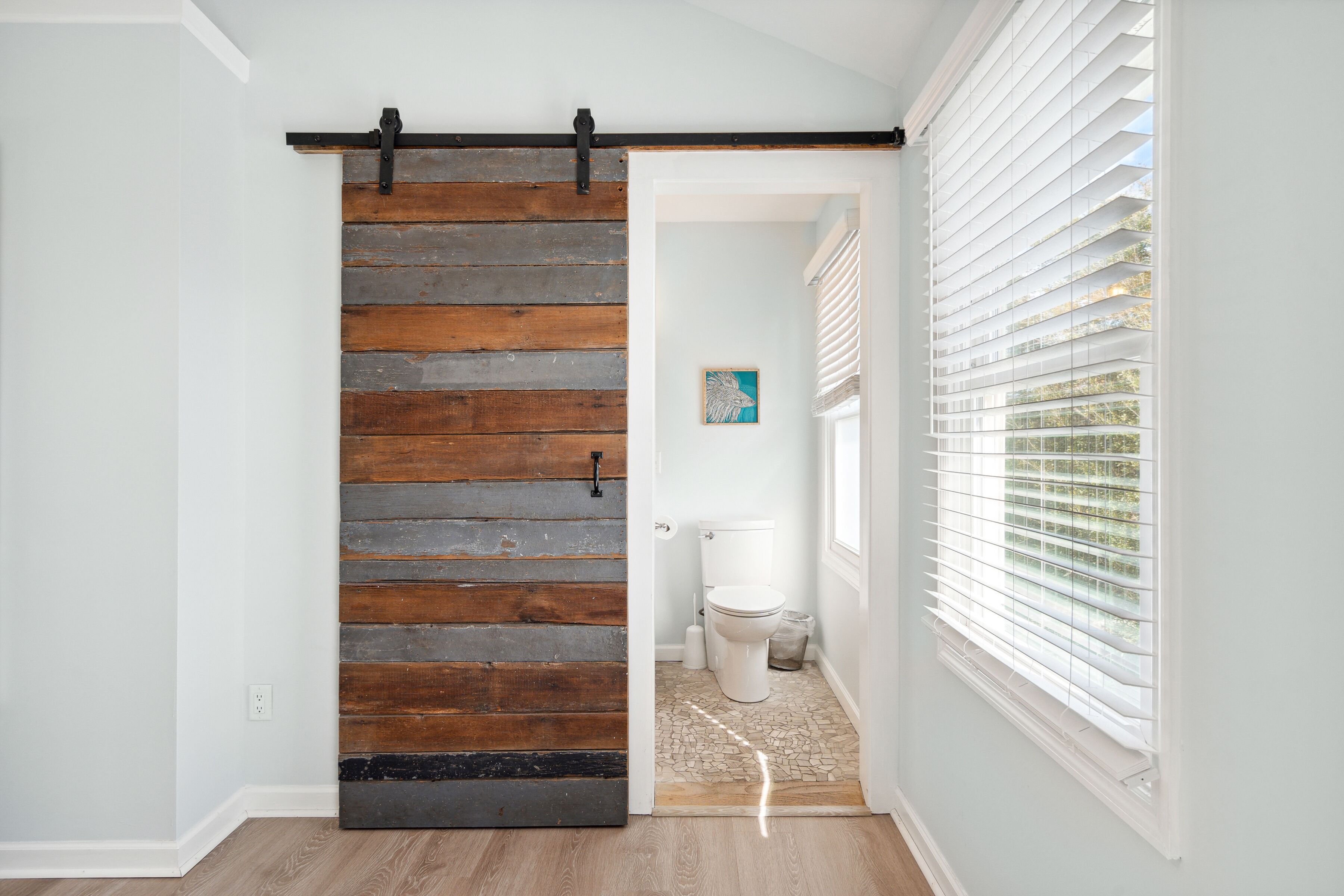 Une salle de bain avec une porte coulissante en bois, des murs blancs et une fenêtre avec des stores.