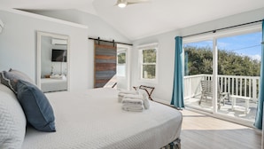 Ein Schlafzimmer mit Bett, Deckenventilator, großem Fenster und einem Balkon mit Blick auf Bäume.