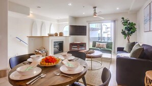 A modern living room with a dining area, a flat-screen TV, and a green sofa.