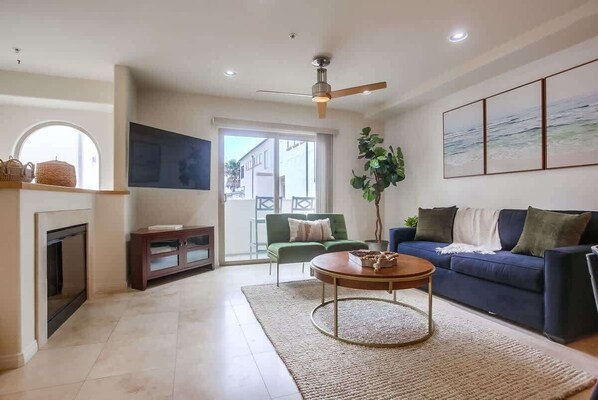 Una sala de estar con chimenea, un sofá verde, un sofá azul, una mesa de centro y un ventanal grande.