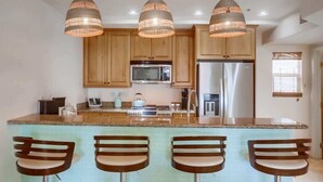 A kitchen with wooden cabinets, stainless steel appliances, a granite countertop, and three pendant lights.