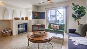 A living room with a fireplace, a ceiling fan, a green sofa, and a large window.