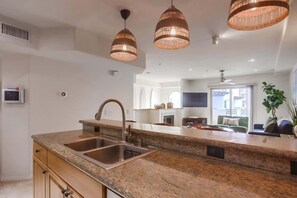 A kitchen with granite countertops, stainless steel sink, and pendant lighting.