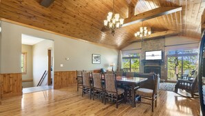 A spacious dining area with a wooden floor and a large table surrounded by chairs. A fireplace is visible in the background, and there is a sign for RentBrinson.com. - Luxurious Adirondack Lodge at Taneycomo with Hot Tub, Stunning Views & Free SDC Tickets (Branson)