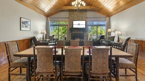 A spacious dining area with a large wooden table and patterned chairs, a stone fireplace, and a television mounted on the wall. - Luxurious Adirondack Lodge at Taneycomo with Hot Tub, Stunning Views & Free SDC Tickets (Branson)