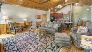 A spacious living room with a wooden ceiling, a large rug, and a kitchen in the background. - Luxurious Adirondack Lodge at Taneycomo with Hot Tub, Stunning Views & Free SDC Tickets (Branson)