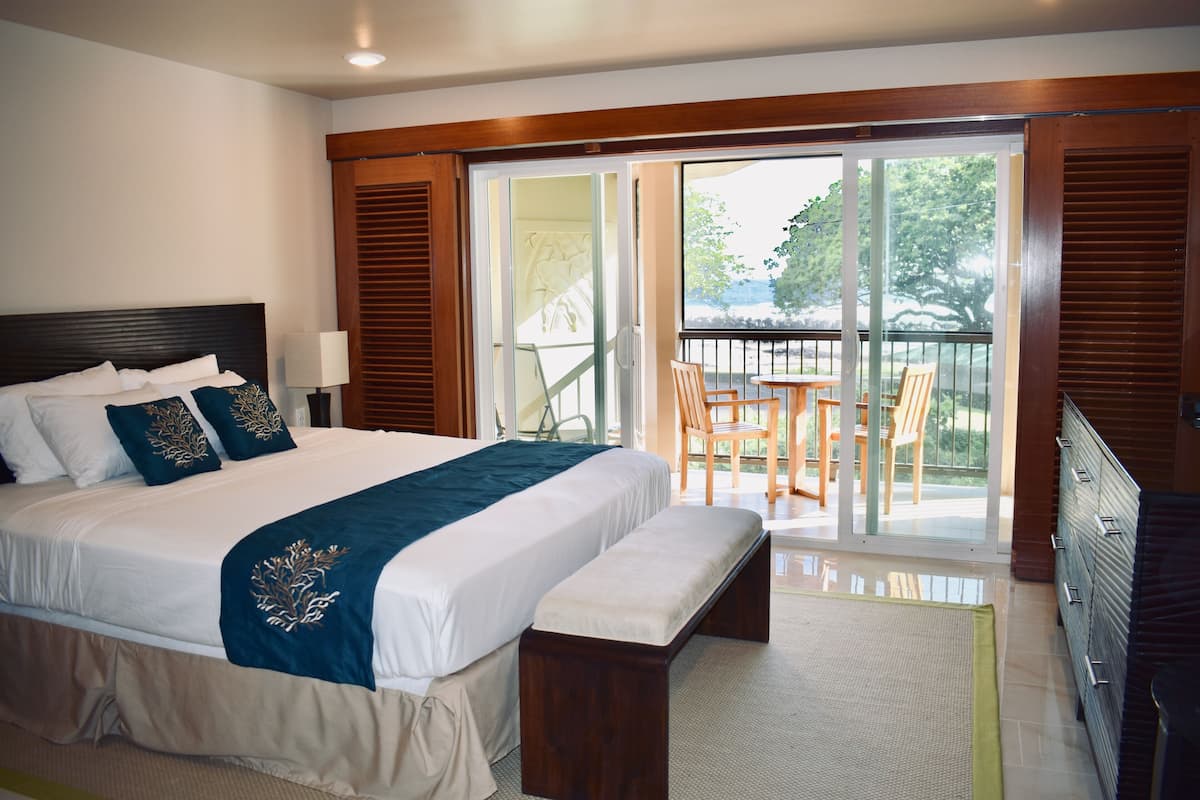 Une chambre d’hôtel avec un grand lit, une banquette, un bureau, une chaise et un balcon équipé d’une table et de chaises.