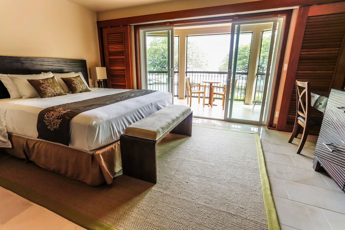 Un grand lit avec une banquette, un bureau et un balcon avec des chaises.
