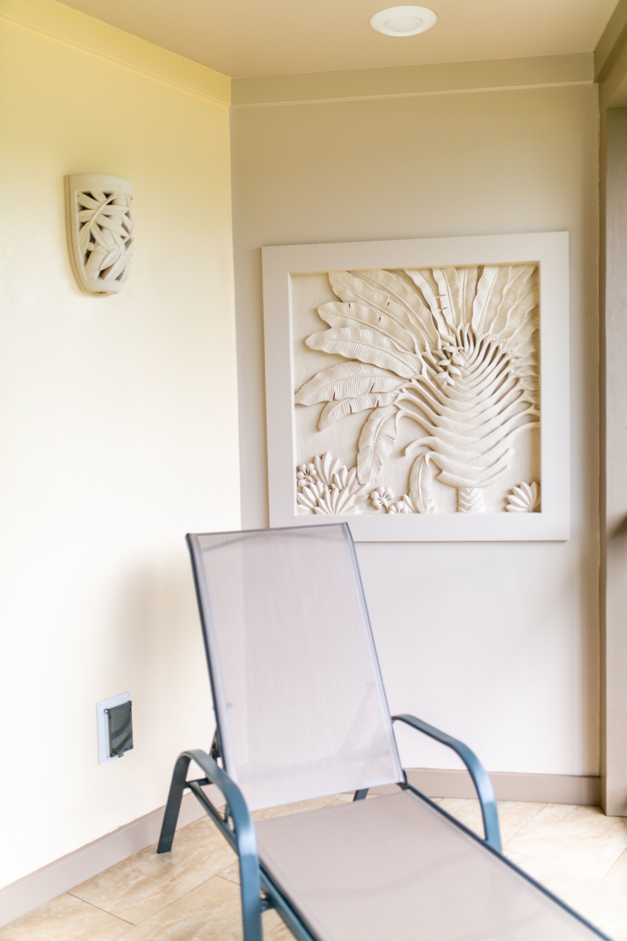 A room with a metal-framed chair, a decorative wall panel, and a light switch on the wall.