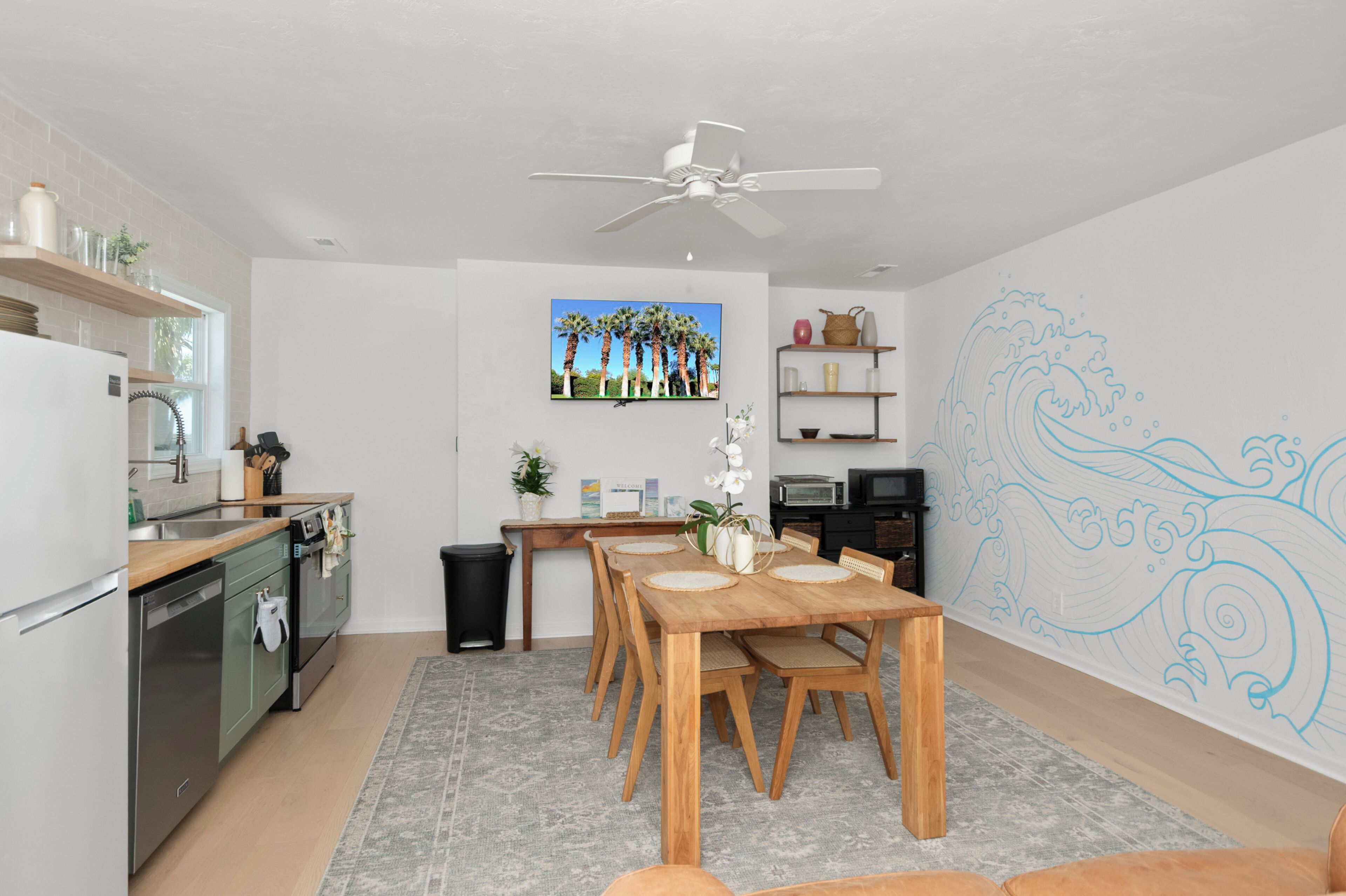 A modern kitchen with a dining area, white walls, and a ceiling fan.
