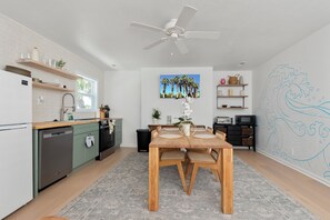 A modern kitchen with a dining area, white walls, and a ceiling fan.