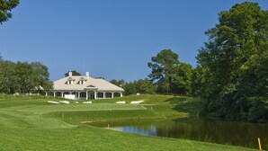 Ein Golfplatz mit Clubhaus, Teich und umliegenden Bäumen.