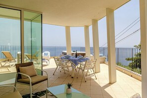 A balcony with a dining table and chairs, a glass door, and a view of the sea. - Karola Suite-Exclusive Stay (Acireale)
