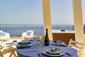 A dining table set with plates, glasses, and cutlery, overlooking a body of water. - Karola Suite-Exclusive Stay (Acireale)