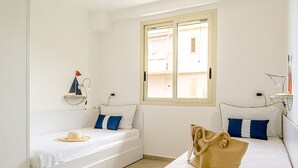 A room with two beds, a window, and a small shelf with a model sailboat. - Suite Home Astrid (Mascali)