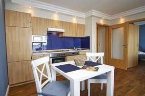 A compact kitchen with wooden cabinets, a microwave, a stove, and a dining area with a white table and chairs. - Die Ferienwohnung Nr. 02 im Haus am Meer - Haus am Meer (Lohme)