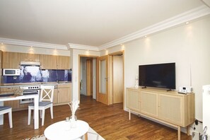A modern apartment with a kitchen, dining area, and living room. It includes a dining table, chairs, a TV, and a small cabinet. - Die Ferienwohnung Nr. 02 im Haus am Meer - Haus am Meer (Lohme)