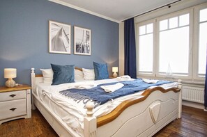 Une chambre à coucher avec un lit, deux tables de chevet, une fenêtre avec des rideaux et deux tableaux encadrés accrochés au mur.