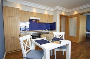 Una cocina compacta con armarios de madera, un microondas, una estufa y una zona de comedor con una mesa y sillas blancas.