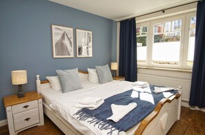 Un dormitorio ordenado con cama, mesitas de noche y una ventana con cortinas.