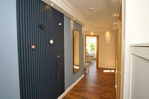 A hallway with a dark blue wall, wooden flooring, and a mirror.