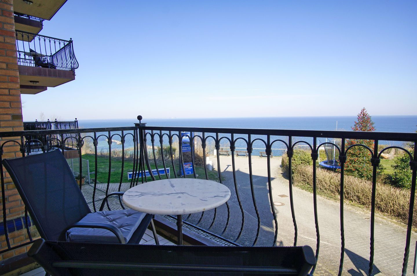 Ein Balkon mit Tisch und Stühlen, der auf eine Küstenlandschaft mit freiem Blick aufs Meer und ein Hinweisschild blickt.