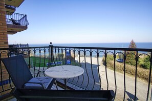 A balcony with a table and chairs, overlooking a coastal area with a clear view of the sea and a signboard.