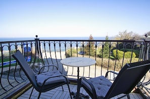 Ein Balkon mit Tisch und zwei Stühlen, der auf ein Gewässer und einen Park Blick bietet.