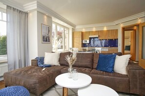 A modern living room with a brown sectional sofa, white round coffee table, and a view of a kitchen and dining area.