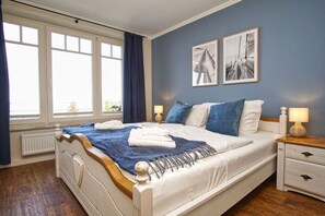 Ein Schlafzimmer mit einem Bett, Nachttischen, einem Fenster und zwei gerahmten Bildern an der Wand.