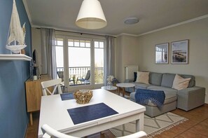 A modern living room with a white table, grey sofa, and a balcony with outdoor seating. - Die Ferienwohnung Nr. 03 im Haus am Meer - Haus am Meer (Lohme)