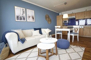 A living room with a sofa, a round table, and a kitchen area with wooden cabinets and a microwave.