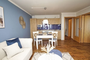 A modern living room with a white sofa, a dining table with chairs, and a kitchen in the background.