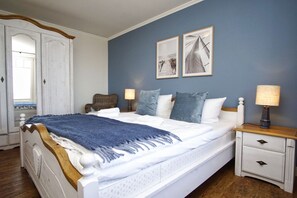 Un dormitorio con una cama grande, dos mesitas de noche, una silla y dos cuadros colgados en la pared.
