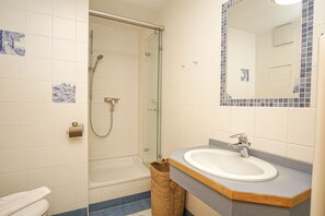 Un baño con ducha envuelta en vidrio, un lavamanos blanco con encimera de madera y un espejo con borde de azulejos azules.