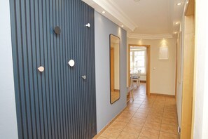A hallway with a blue wall featuring vertical lines and circular wall decorations, leading to a dining area with a window and a door. - Die Ferienwohnung Nr. 04 im Haus am Meer - Haus am Meer (Lohme)