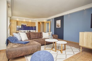 A modern living room with a brown sectional sofa, two white round tables, and a blue knitted pouf. - Die Ferienwohnung Nr. 04 im Haus am Meer - Haus am Meer (Lohme)