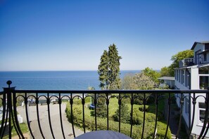 Ein Balkon mit Blick auf das Meer, ein hoher Baum und ein Gebäude mit Balkon.