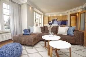 Ein modernes Wohnzimmer mit einem braunen Ecksofa, zwei weißen runden Tischen und einem blauen Strickponton.