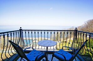 Un balcon avec une table et deux chaises, donnant sur une marina où sont amarrés des bateaux, et offrant une vue dégagée sur la mer.