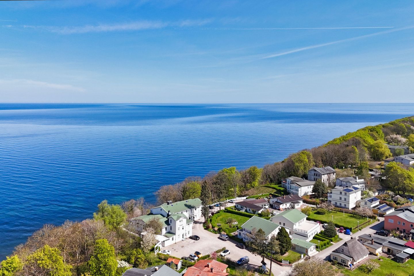 Une zone résidentielle côtière, avec des maisons, une mer d’un bleu limpide et un paysage vallonné.