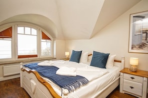 Ein Schlafzimmer mit einem Bett, zwei Nachttischen, einem Fenster mit Jalousien und einem gerahmten Bild an der Wand.